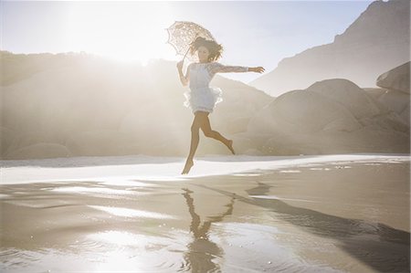 simsearch:649-08543884,k - Woman leaping on beach wearing short white dress holding umbrella Fotografie stock - Premium Royalty-Free, Codice: 649-08543857