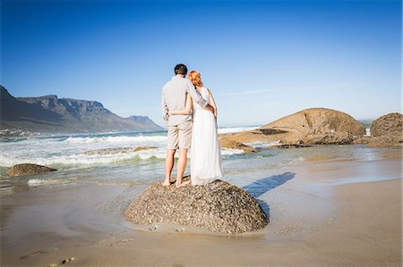 simsearch:696-03402108,k - Full length rear view of couple, arms around eachother, standing on rock on coastline Stock Photo - Premium Royalty-Free, Code: 649-08543874