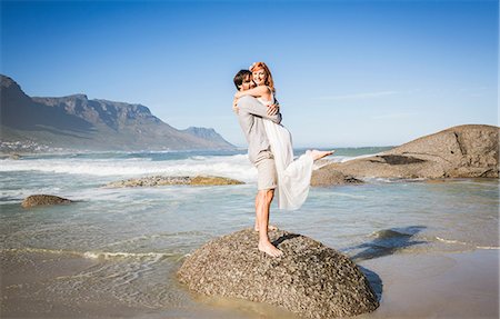 simsearch:649-08543868,k - Full length side view of man standing on rock lifting woman, looking at camera smiling Stock Photo - Premium Royalty-Free, Code: 649-08543875