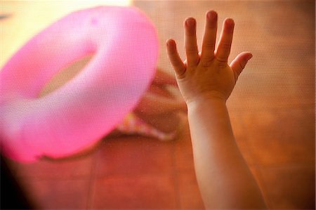pink inner tube - Child's hand touching mesh screen, pink inflatable ring in background Stock Photo - Premium Royalty-Free, Code: 649-08562439