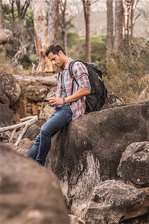 Male hiker reading smartphone texts on forest rock formation, Deer Park, Cape Town, South Africa Stock Photo - Premium Royalty-Free, Code: 649-08576282