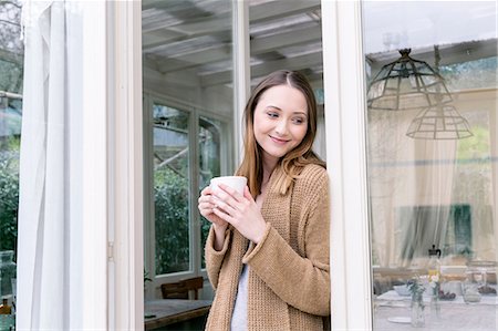 Woman leaning against doorway holding coffee cup looking away smiling Photographie de stock - Premium Libres de Droits, Code: 649-08576322