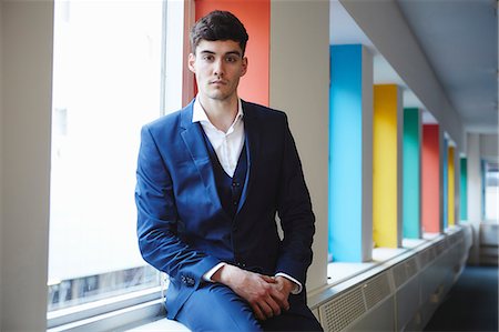 Man wearing suit sitting on windowsill looking at camera Stock Photo - Premium Royalty-Free, Code: 649-08576338