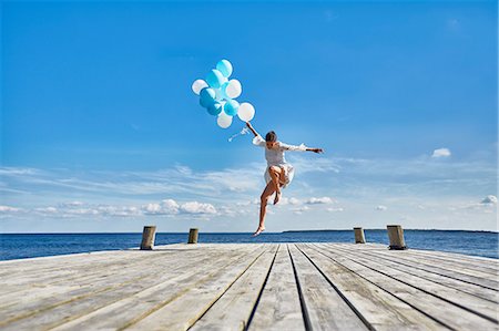 dock jumping - Young woman dancing on wooden pier, holding bunch of balloons Stock Photo - Premium Royalty-Free, Code: 649-08576429