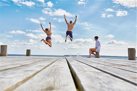 Young woman sitting on post on wooden pier, watching friends as they jump into sea Stock Photo - Premium Royalty-Free, Code: 649-08576437