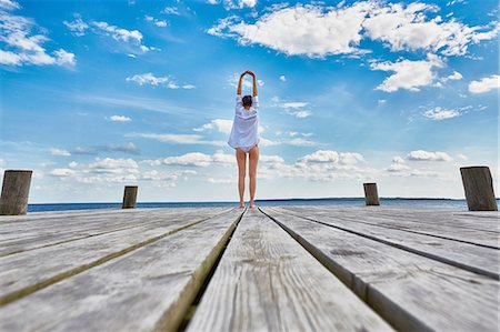 simsearch:649-08232578,k - Young woman standing on wooden pier, stretching, rear view Stock Photo - Premium Royalty-Free, Code: 649-08576433