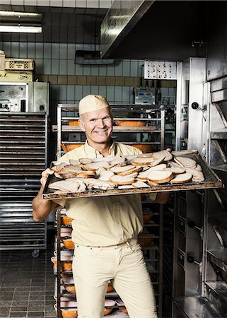 Happy baker placing tray of sliced bread into oven Stock Photo - Premium Royalty-Free, Code: 649-08576652