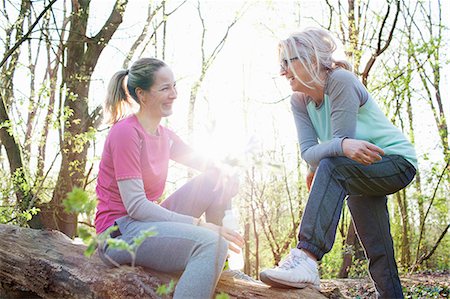 simsearch:649-08381348,k - Women in forest sitting on fallen tree face to face smiling Fotografie stock - Premium Royalty-Free, Codice: 649-08576854