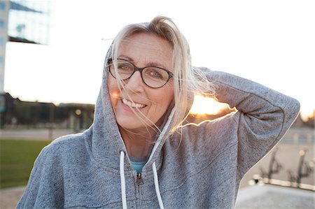 Portrait of woman wearing eyeglasses and hooded top looking at camera smiling Stock Photo - Premium Royalty-Free, Code: 649-08576872