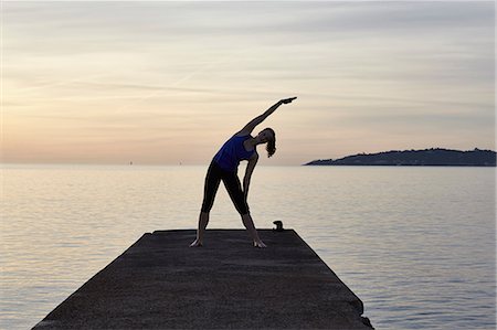 simsearch:649-08577001,k - Young woman standing on pier, in yoga position, at sunset Fotografie stock - Premium Royalty-Free, Codice: 649-08576998