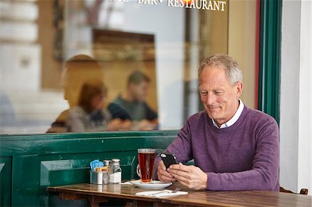 simsearch:649-08824700,k - Mature man reading smartphone text at sidewalk cafe table Foto de stock - Royalty Free Premium, Número: 649-08577191