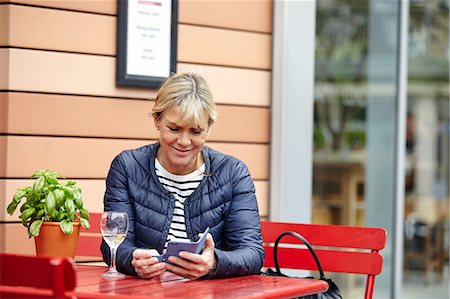 simsearch:649-08824700,k - Mature woman reading smartphone texts at sidewalk cafe Foto de stock - Royalty Free Premium, Número: 649-08577207