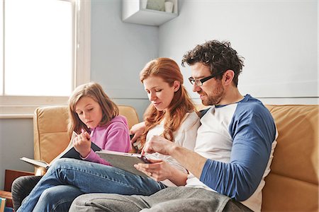 simsearch:649-08577535,k - Mid adult parents and daughter on sofa concentrating on reading book and digital tablet Stock Photo - Premium Royalty-Free, Code: 649-08577235