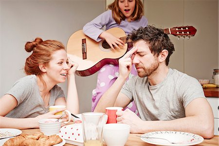 Tired mid adult parents at breakfast table whilst daughter plays guitar Stock Photo - Premium Royalty-Free, Code: 649-08577230