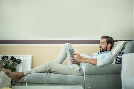 Young man reclining on hotel room chaise longue using digital tablet, Dubai, United Arab Emirates Foto de stock - Sin royalties Premium, Código: 649-08577538