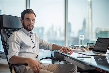 Portrait of businessman at desk with window view of Burj Khalifa, Dubai, United Arab Emirates Stock Photo - Premium Royalty-Free, Code: 649-08577540