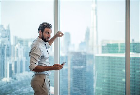 Businessman reading smartphone text at window with view of Burj Khalifa, Dubai, United Arab Emirates Foto de stock - Sin royalties Premium, Código: 649-08577542