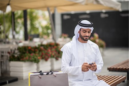 shopper texting - Male shopper  wearing traditional middle eastern clothing sitting on bench reading smartphone text, Dubai, United Arab Emirates Stock Photo - Premium Royalty-Free, Code: 649-08577555