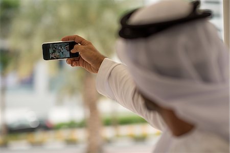 Over shoulder of middle eastern man taking smartphone selfie with friends at cafe, Dubai, United Arab Emirates Stock Photo - Premium Royalty-Free, Code: 649-08577567