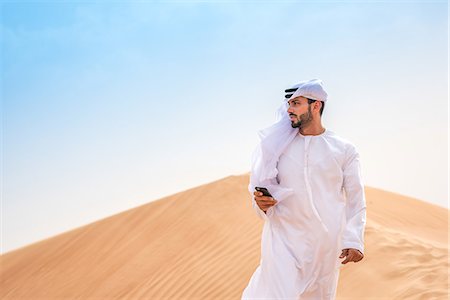 Middle eastern man wearing traditional clothes using smartphone on desert dune, Dubai, United Arab Emirates Photographie de stock - Premium Libres de Droits, Code: 649-08577575