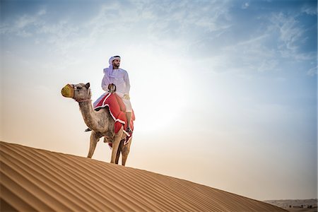 Man wearing traditional middle eastern clothes riding camel in desert, Dubai, United Arab Emirates Stock Photo - Premium Royalty-Free, Code: 649-08577596