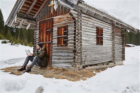 elmau - Young man reading map sitting outside log cabin in winter, Elmau, Bavaria, Germany Foto de stock - Royalty Free Premium, Número: 649-08577717