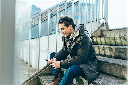 simsearch:649-08562431,k - Man sitting on step using smartphone smiling Stock Photo - Premium Royalty-Free, Code: 649-08577895