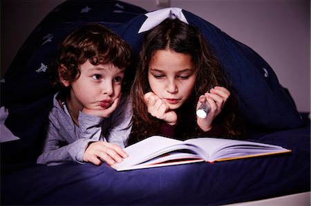simsearch:649-07064289,k - Brother and sister under duvet reading book by torchlight Photographie de stock - Premium Libres de Droits, Code: 649-08577932