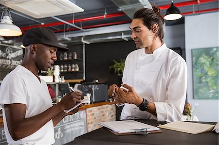 restaurant interior chalkboard - Employee in restaurant talking with chef, making notes in notebook Stock Photo - Premium Royalty-Free, Code: 649-08578056