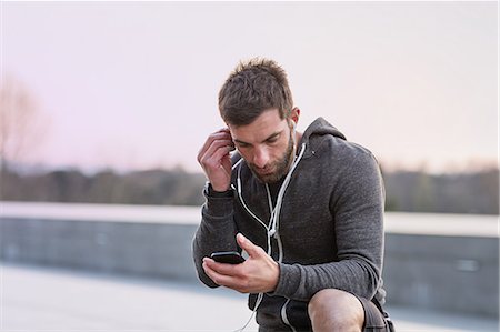 Mid adult man, outdoors, looking at smartphone, wearing earphones Fotografie stock - Premium Royalty-Free, Codice: 649-08660575