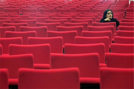 sad and quiet woman - Woman sitting alone in hall of empty red seats Stock Photo - Premium Royalty-Free, Code: 649-08661097