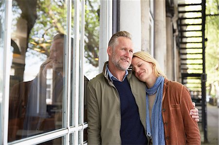 simsearch:649-08661396,k - Mature couple leaning against window smiling Photographie de stock - Premium Libres de Droits, Code: 649-08661392