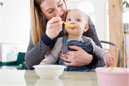 simsearch:649-08661494,k - Mid adult woman feeding baby daughter at kitchen table Fotografie stock - Premium Royalty-Free, Codice: 649-08661487