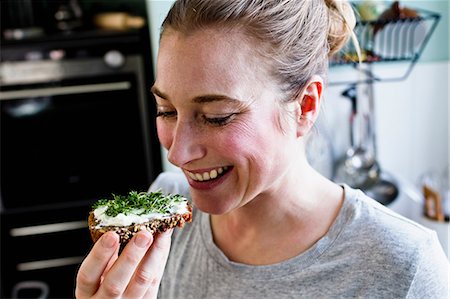 eating smile - Mid adult woman eating rye bread snack in kitchen Stock Photo - Premium Royalty-Free, Code: 649-08661531