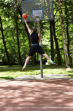 Rear view of young male basketball player jumping and throwing ball at hoop Stock Photo - Premium Royalty-Free, Code: 649-08661716
