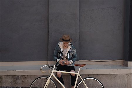 sombrero de fieltro - Young man sitting on wall, bike in front of him, using smartphone Foto de stock - Sin royalties Premium, Código: 649-08662046