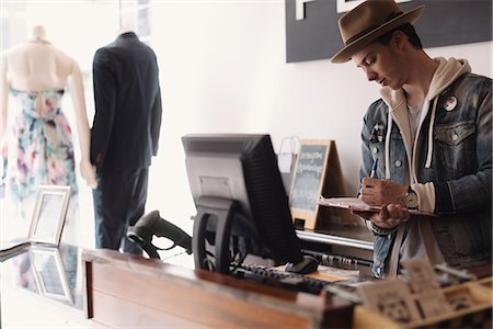 fashion and retail salesman - Young male shop worker standing behind counter, making notes Stock Photo - Premium Royalty-Free, Code: 649-08662040