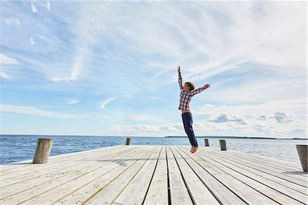 sweden fun - Young boy on wooden pier, jumping to reach bubbles Stock Photo - Premium Royalty-Free, Code: 649-08702231