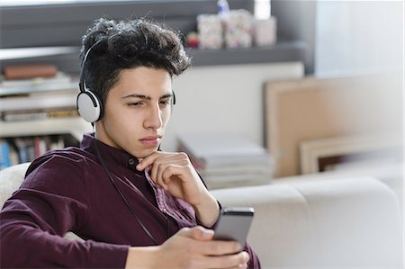 simsearch:649-08702598,k - Young man on sofa wearing headphones holding smartphone Stock Photo - Premium Royalty-Free, Code: 649-08702597