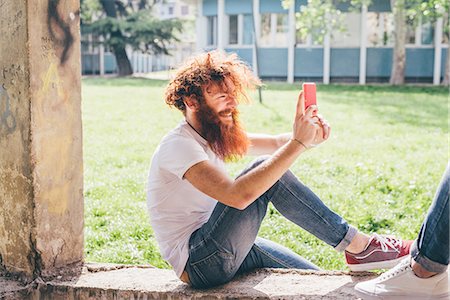 simsearch:649-08765972,k - Young male hipster with red hair and beard photographing friend on smartphone in park Photographie de stock - Premium Libres de Droits, Code: 649-08702628