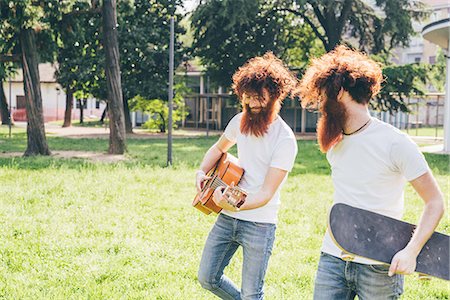 simsearch:649-08765972,k - Young male hipster twins with red hair and beards strolling in park playing guitar Fotografie stock - Premium Royalty-Free, Codice: 649-08702636