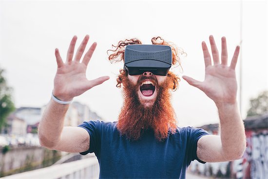 Portrait of young male hipster with red hair and beard screaming whilst wearing virtual reality headset Stock Photo - Premium Royalty-Free, Image code: 649-08702681