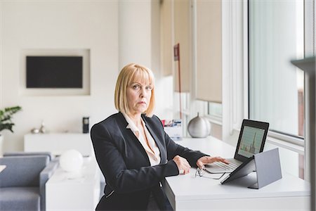 simsearch:6124-08520431,k - Portrait of mature businesswoman using digital tablet and laptop at office desk Stock Photo - Premium Royalty-Free, Code: 649-08702848