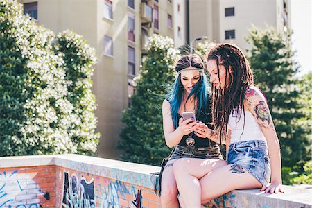 Two young women on wall reading smartphone texts in urban housing estate Stock Photo - Premium Royalty-Free, Code: 649-08703296
