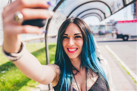 simsearch:649-08703311,k - Young woman with dip dyed blue hair taking smartphone in urban bus shelter Foto de stock - Sin royalties Premium, Código: 649-08703313