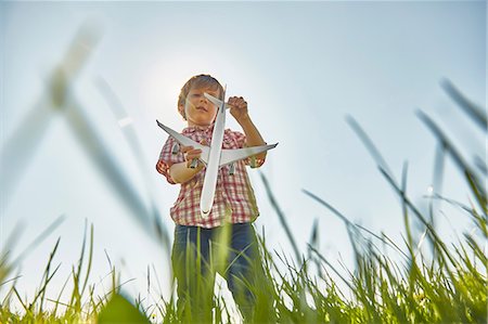 simsearch:649-08702598,k - Low angle view of boy standing in grass checking toy airplane tail Stock Photo - Premium Royalty-Free, Code: 649-08714082