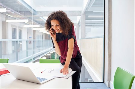 smartphone laptop - Female designer reading laptop and talking on smartphone  in design studio Stock Photo - Premium Royalty-Free, Code: 649-08714121