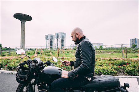 Mature male motorcyclist sitting on motorcycle reading smartphone text Fotografie stock - Premium Royalty-Free, Codice: 649-08714739