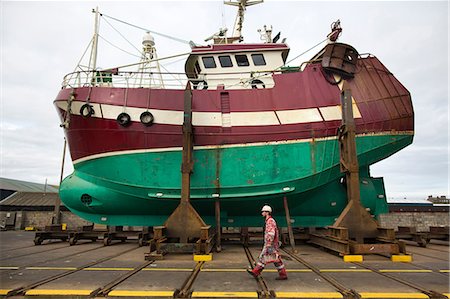 fishing boats scotland - Male ship painter walking in front of fishing boat on drydock Stock Photo - Premium Royalty-Free, Code: 649-08715021