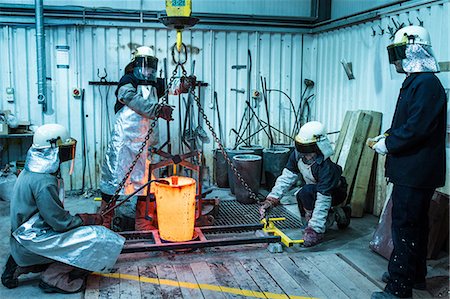 Male foundry workers winching bronze melting pot in bronze foundry Stock Photo - Premium Royalty-Free, Code: 649-08715036